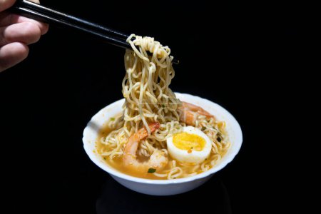 Spicy instant noodle with shrimp and egg on black background.