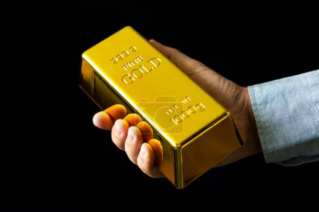 Téléchargez les photos : Un homme tient de l'or sur un fond noir. Présenter 1000 g de lingots d'or fin - en image libre de droit