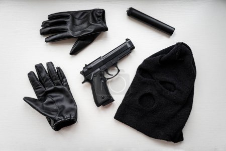 Photo for Gloves, a pistol and a black mask on a white table. Evidence during the search of a robber or murderer. evidence of a crime. - Royalty Free Image