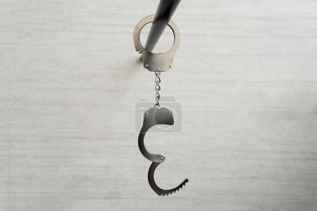 Photo for Handcuffs hanging on black pipe near white wall indoors. concept of arrest of unfreedom or sexual role-playing games of bdsm. - Royalty Free Image