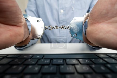 Geschäftsmannhand mit Handschellen und Computer-Laptop. Das Konzept der Verbrechen im Cyberspace.
