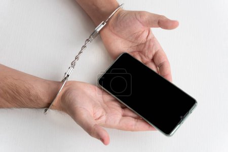 Photo for Handcuffs man's hands and mobile phone. Concept of addiction. a phone fraudster in handcuffs with a smartphone. right to call - Royalty Free Image