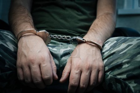 military soldier in handcuffs, hands behind his back, on a dark background. Concept: war criminal, prisoner of war, tribunal. a prisoner of war under interrogation.