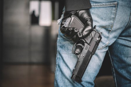 Photo for Robber in a black glove holds a gun in his hand. weapon for your self defense. a man takes a gun out of his pocket, the concept of self-defense or suppression, robbery. Legalization of firearms. - Royalty Free Image