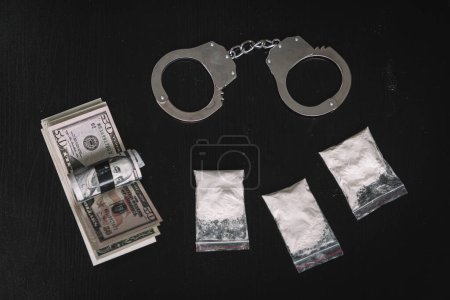 Betäubungspulver in einem Geldbeutel und Handschellen auf schwarzem Hintergrund des Tisches. Das Konzept des Drogenhandels oder Drogenhandels.