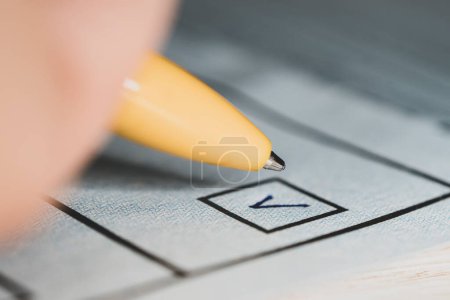 Écrire une case à cocher avec un stylo sur papier - Chaque vote compte Concept, une marque dans la sélection et un stylo gros plan. une case à cocher pour voter. Élections présidentielles ou législatives