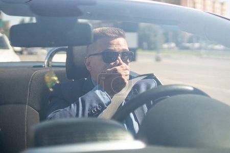 Téléchargez les photos : Conducteur choqué dans la voiture. Un homme d'affaires conduisant une voiture se couvre la bouche avec sa main, une émotion de surprise ou de choc. Accident de la route. - en image libre de droit