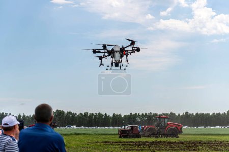 Téléchargez les photos : Drone agricole pulvériser un champ. les agriculteurs regardent et contrôlent à distance un drone pour la transformation des champs. - en image libre de droit