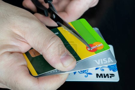 Photo for April 2, 2022. Barnaul. Russia: a man cuts bank credit cards of the type and mastercard with scissors. Destruction of plastic cards after the expiration date. - Royalty Free Image
