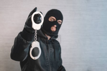 Photo for A bandit in a black mask and gloves with handcuffs in his hands on a white background. Release from imprisonment. Prison break concept. Jailbreak - Royalty Free Image