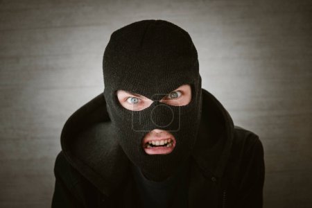 Photo for A thief in a black jacket. A man in a black balaclava with an evil expression on his face. An aggressive bandit on a white background. The concept of crime or theft. - Royalty Free Image
