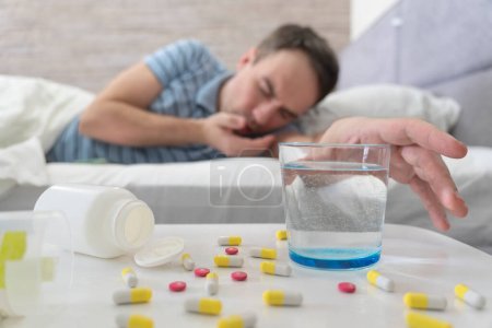 Resaca. El hombre toma Píldora y Agua. Hombre en la cama Dolor de cabeza matinal. Hombre usando aspirina. Un vaso de agua en primer plano. síntoma es intoxicación alimentaria.