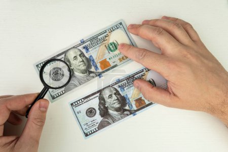 Photo for Counterfeiter forges banknotes. Fake concept. Fake money American dollars, magnifier. view money under a magnifying glass. watermark, water mark. search for counterfeit bills - Royalty Free Image