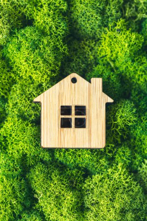 Casa de madera en miniatura sobre musgo verde. El concepto de venta, seguro o alquiler de bienes raíces. foto vertical