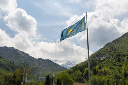 Photo for The flag of the Republic of Kazakhstan on top of mountain, against a background of blue sky with white clouds. - Royalty Free Image