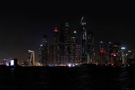 Foto de El horizonte de Dubai Marina después del atardecer con un mar en primer plano. Hermosa vista nocturna de los rascacielos de Dubai desde el mar. - Imagen libre de derechos