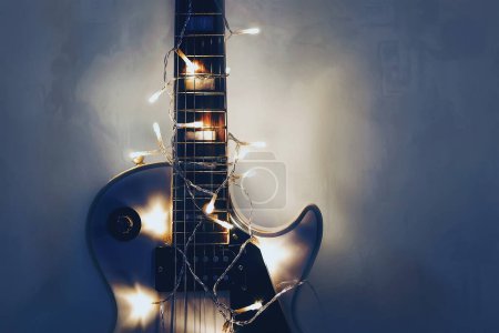Foto de Guitarra eléctrica con guirnalda iluminada sobre fondo oscuro. Guitarra regalo formas clásicas para Navidad o año nuevo
. - Imagen libre de derechos