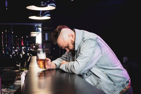 Foto de Un hombre borracho y brutal con un cóctel alcohólico en una copa. El concepto de malos hábitos y adicción al alcohol. Hombre triste solitario se emborracha en un pub irlandés - Imagen libre de derechos