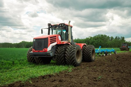 Téléchargez les photos : Tracteur rouge travaillant dans un champ par une journée ensoleillée. concept de travail dans les domaines et l'agriculture. - en image libre de droit