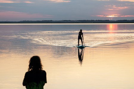 Photo for Side view silhouette of alone male paddle boarder in sunset. Paddle-boarding in bay. During sunset, one young man, paddleboarding with stand up paddle board on a lake. - Royalty Free Image