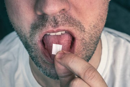Foto de Hombre con LSD en la lengua. fondo negro. un sello blanco con ácido narcótico en la lengua. - Imagen libre de derechos