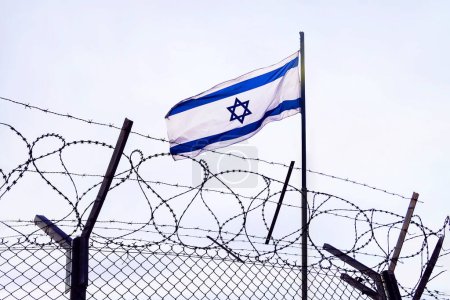 Foto de Vista de la bandera israelí detrás de alambre de púas contra el cielo nublado. puesto fronterizo en la frontera de Israel. El puesto de control de la embajada del país. la frontera palestino-israelí. - Imagen libre de derechos