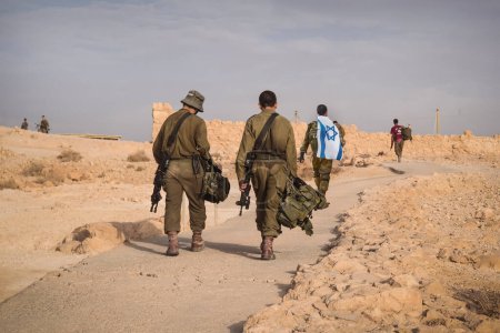 Rückenschuss von mehreren Soldaten der israel Armee, die mit einer israel Nationalflagge laufen. Militärangehöriger geht mit anderen Soldaten spazieren. Kriegstaktische Übung. Infanterie zieht sich aus Stellungen zurück