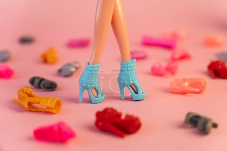Foto de Piernas de muñeca de plástico y una casa entre una variedad de zapatos de colores. el concepto del desarrollo del culto al consumo en los niños. - Imagen libre de derechos