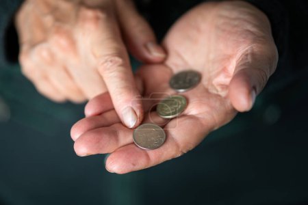 Photo for Elderly woman counts coins, wrinkled female hands with metal money closeup. Concept of poverty, pension payments, retiree. old women's hands count coins. - Royalty Free Image
