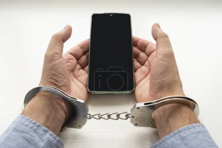 Photo for Handcuffs man's hands and mobile phone. Concept of addiction. a phone fraudster in handcuffs with a smartphone. - Royalty Free Image