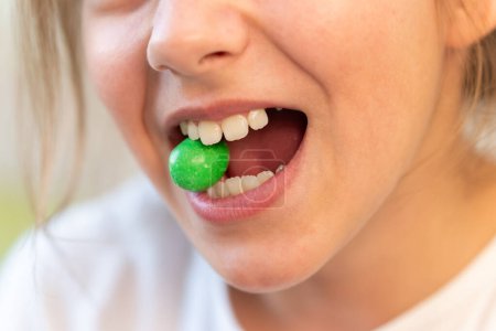 Foto de Un caramelo verde redondo en los dientes de una joven adolescente. Adicción de dulces y caramelos. El daño de los dulces para los dientes. - Imagen libre de derechos