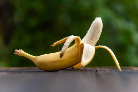 Composition of fresh fruits, whole fresh tasty banana without skin against a blurred background of nature