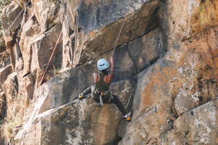 Eine junge Afroamerikanerin klettert an einer Granitklippe entlang. das Mädchen hält sich am Sicherungsseil für den Abstieg von der Klippe fest.