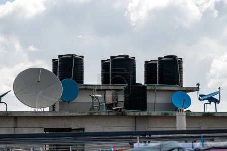 Téléchargez les photos : Réservoir d'eau sur le toit au ciel bleu. Réservoir d'eau noire sur le toit d'un grand bâtiment contre un ciel bleu. Méthode de chauffage de l'eau dans les pays du Sud. Eau de chauffage de l'énergie solaire en Inde - en image libre de droit