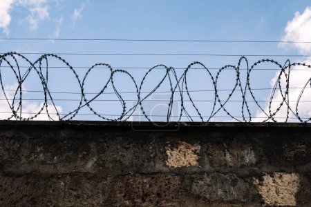 Betonsteinmauer mit Stacheldraht an geschützter Stelle. Sicherheit, Internierungslager, Konzentrationslager, Gefängniseinrichtung, Strafvollzugs- und Freiheitskonzepte