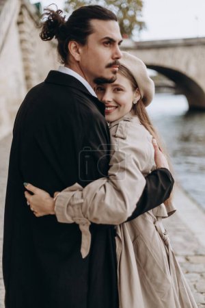 Ein verliebtes Paar spaziert durch die Straßen von Paris, ein Mann in Mantel und Anzug, ein Mädchen in einem Kleid mit Baskenmütze und Trenchcoat im Herbst