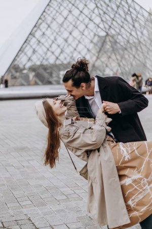 Foto de Una pareja enamorada camina por las calles de París, un tipo con abrigo y traje, una chica con vestido con boina y abrigo en otoño - Imagen libre de derechos
