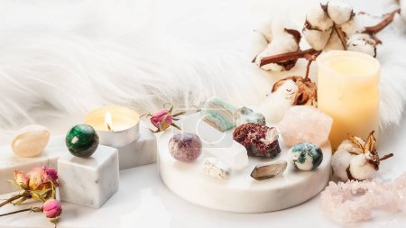 Photo for Minerals Collection on White Marble Stand with Burning Candles and Dry Flowers. Healing Stones for Wicca Witchcraft Practice. Copy Space for Text - Royalty Free Image