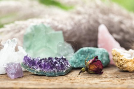 Crystal Healing Stones with Blurred Background and Focus on the Purple Amethyst. Gemstones for Esoteric Spiritual Practice or Witchcraft Set Up on Wooden Table with Dry Herbs and Flowers.