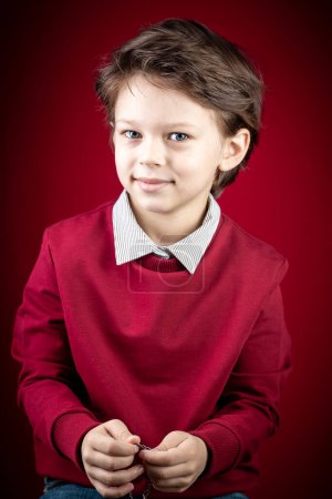 Foto de Close up Portrait of Him He Handsome Cute Smiling Smart Caucasian White Boy Dressed in a Red Pullover and Grey Shirt over Dark Red Background - Imagen libre de derechos