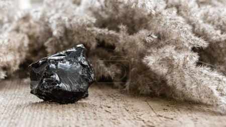 Téléchargez les photos : Piece of raw uncut black opal stone on wooden background. Black opal is rare and expensive gemstone - en image libre de droit