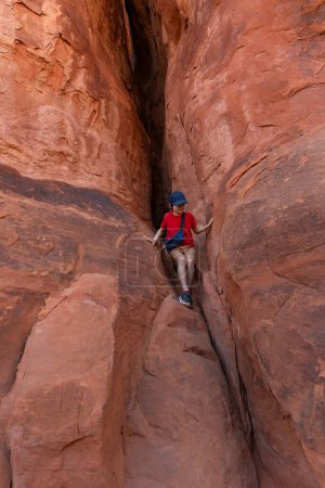 Young Hiker Boy Climbing Rock in Arches National Park, Utah, United States.