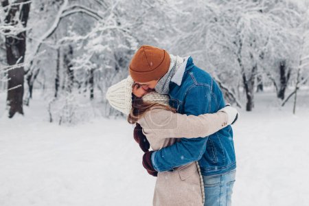Photo for Young stylish loving couple kissing in winter park. Man and woman hugging while walking and enjoying snowy weather outdoors under falling snow. Valentine's day - Royalty Free Image
