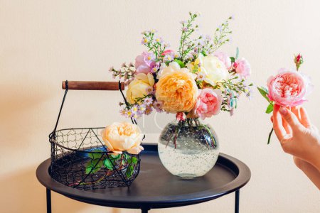 Téléchargez les photos : Gros plan de roses fraîches anglaises. Femme fait bouquet dans un vase transparent avec des fleurs orange jaune rose sur la table à la maison. Décor intérieur - en image libre de droit