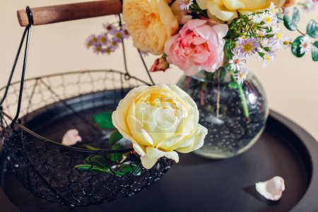 Téléchargez les photos : Bouquet frais de fleurs de roses mis dans un vase en verre sur la table. Gros plan de fleurs jaunes roses avec panier. Décor intérieur d'été - en image libre de droit