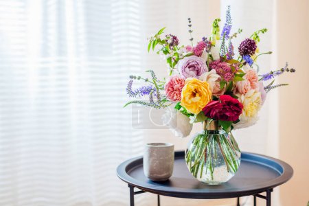 Großaufnahme eines sommerlichen Rosenstraußes, der in einer durchsichtigen Vase auf dem Tisch vor dem Fenster steht. Gemütliche Einrichtung und Dekoration zu Hause. Weltraum