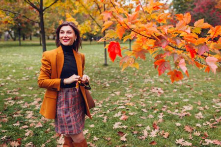 Retrato de una mujer joven y feliz con blazer naranja sosteniendo el bolso relajándose en el parque de otoño. Caer traje femenino. Mira a la moda. Espacio