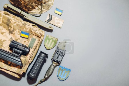 Ukrainian military gear flat lay background. Army tactical uniform clothes, accessories, thermal imager, ammunition, knives with national flags and emblem chevrons. Flat lay, space