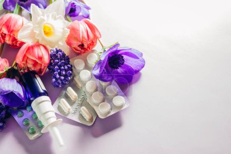 Seasonal spring allergy. Antihistamine pills and nasal spray flat lay with purple pink flowers. Healthcare and medicine. Top view. Space