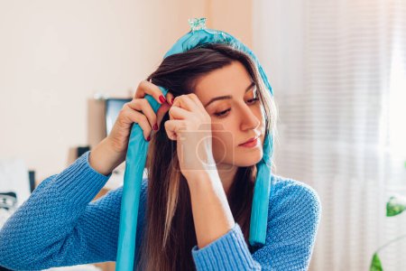 Heatless hair curler. Close up portrait of young woman doing hair at home using headband and claw clip. Beauty products for hairstyle.
